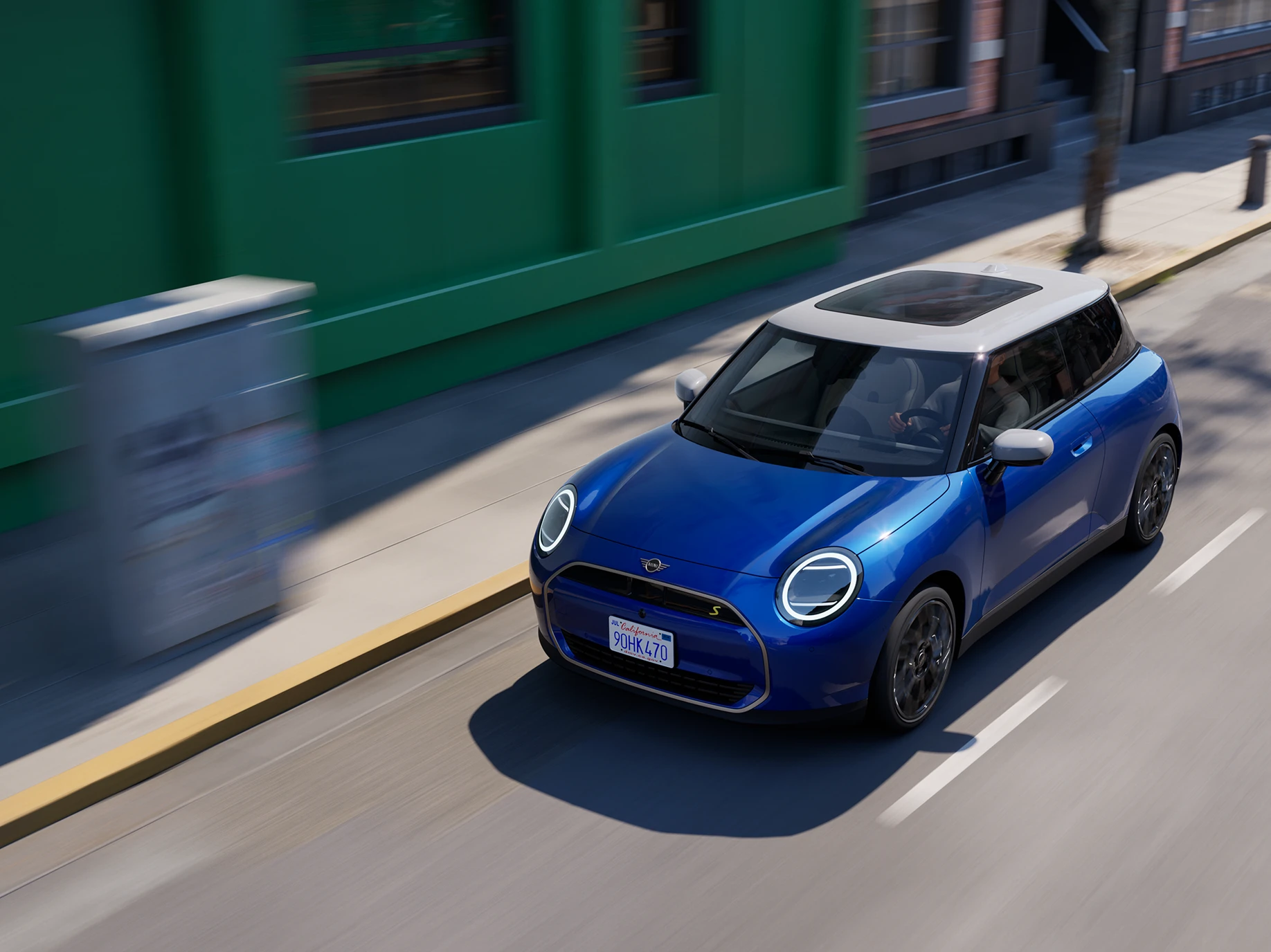 Top view of the all-electric MINI Cooper in Blazing Blue and White Roof driving on a street. 