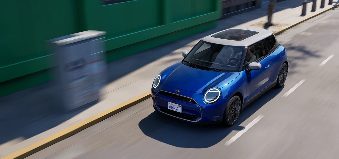 Top view of the all-electric MINI Cooper in Blazing Blue and White Roof driving on a street. 